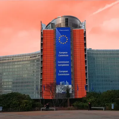 Berlaymont-Gebäude der Europäischen Kommission in Brüssel mit großem blauen EU-Banner vor orangefarbenem Abendhimmel.