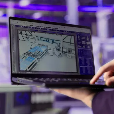 Person nutzt Laptop mit digitalem Fabrikmodell zur Planung oder Überwachung einer Produktionsanlage.