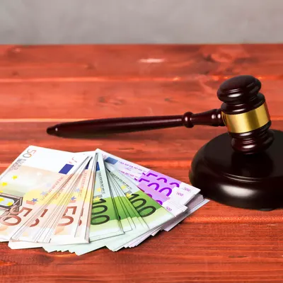 Judge’s gavel next to a stack of euro banknotes on a wooden table, symbolizing legal fines or financial penalties.