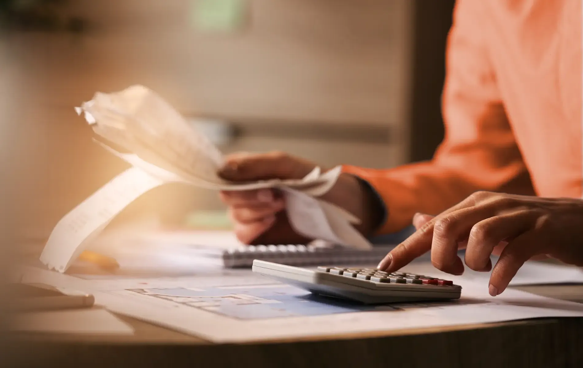 Person prüft Belege und berechnet Ausgaben mit einem Taschenrechner