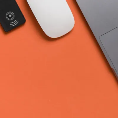 Minimalist setup with a laptop, computer mouse, and RFID device on an orange background