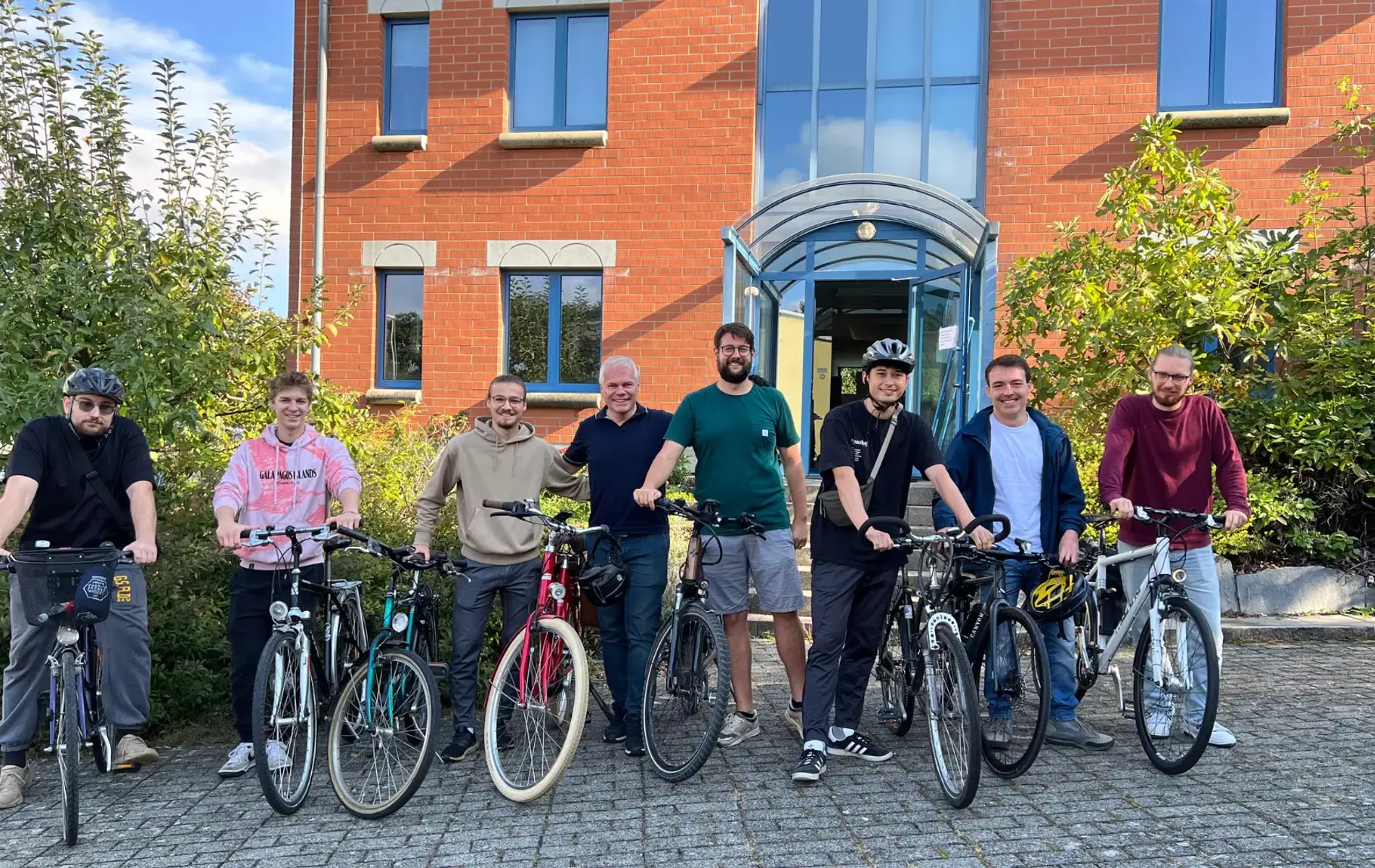 OriginStamp-Team steht mit Fahrrädern vorm Bürogebäude und posiert für ein Gruppenfoto