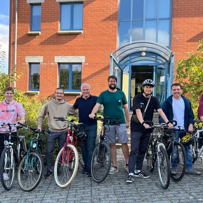 OriginStamp-Team steht mit Fahrrädern vorm Bürogebäude und posiert für ein Gruppenfoto