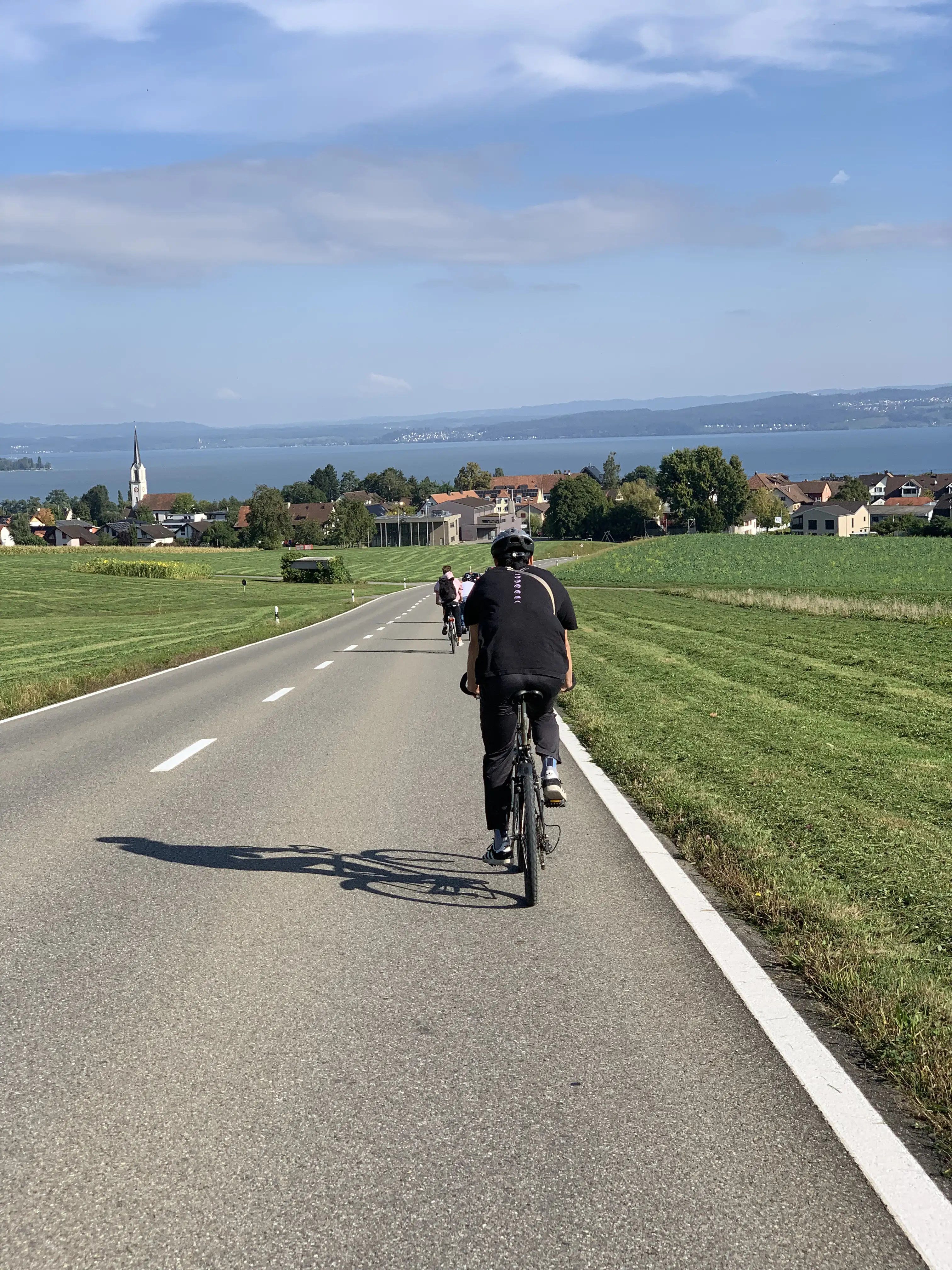 Mitarbeitende auf Fahrrädern bei einer Teambuilding-Tour am Bodensee mit Blick auf See, Kirche und Landschaft