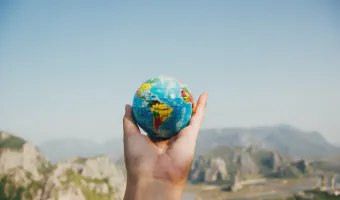 Person Holding World Globe Facing Mountain