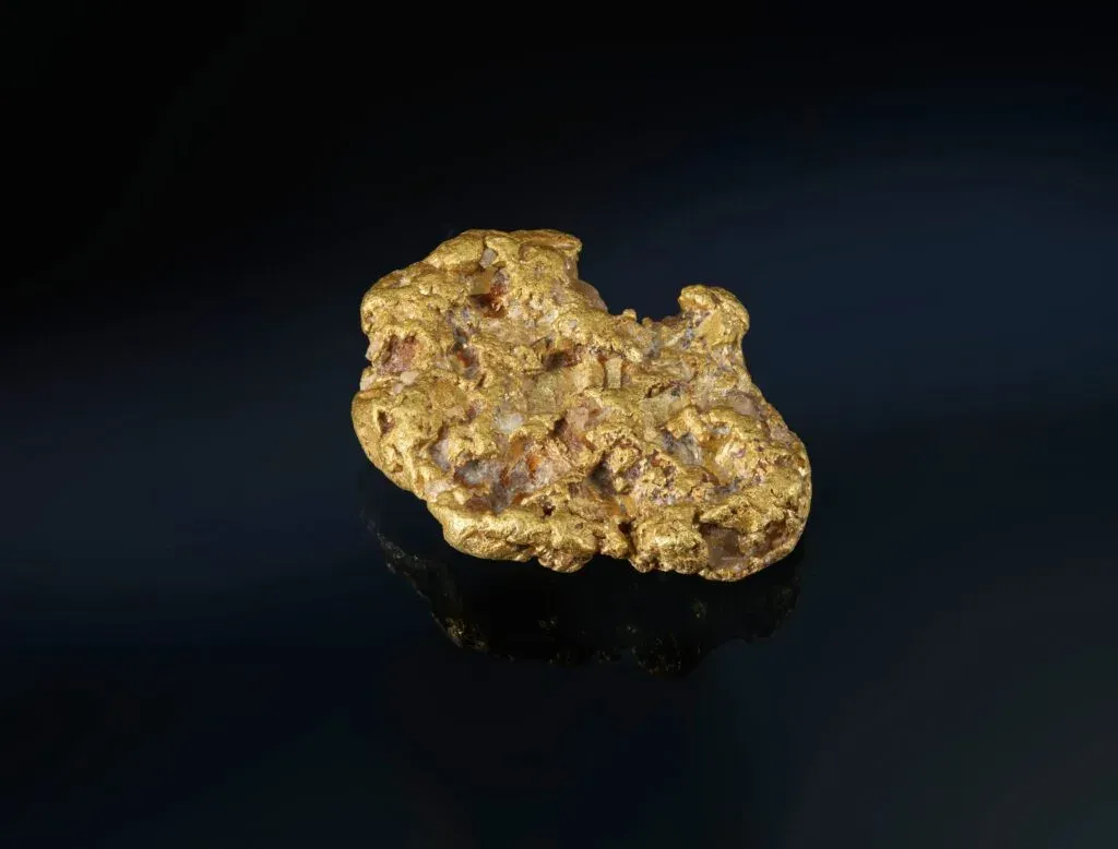 Raues Goldnugget auf einem dunklen, spiegelnden Untergrund.