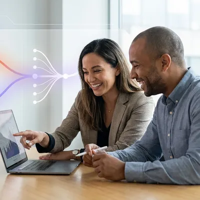 Two smiling colleagues analyzing data on a laptop, with a digital network diagram overlay.
