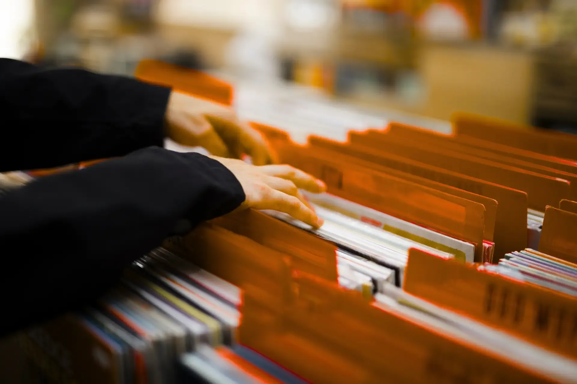 Hände einer Person, die in einer Kiste mit Schallplatten stöbert.