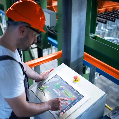 Ein Arbeiter mit Schutzhelm bedient einen Touchscreen einer Fabrikmaschine.