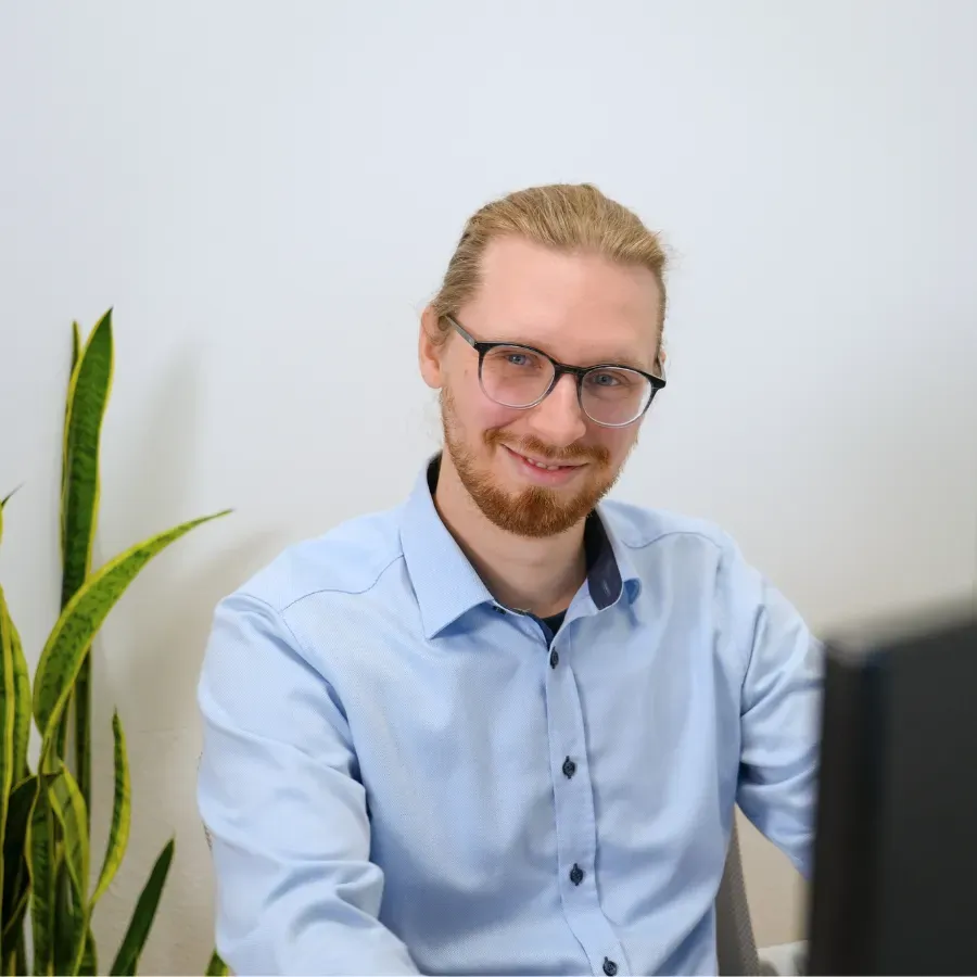 A man is smiling while working at a computer in a bright office.