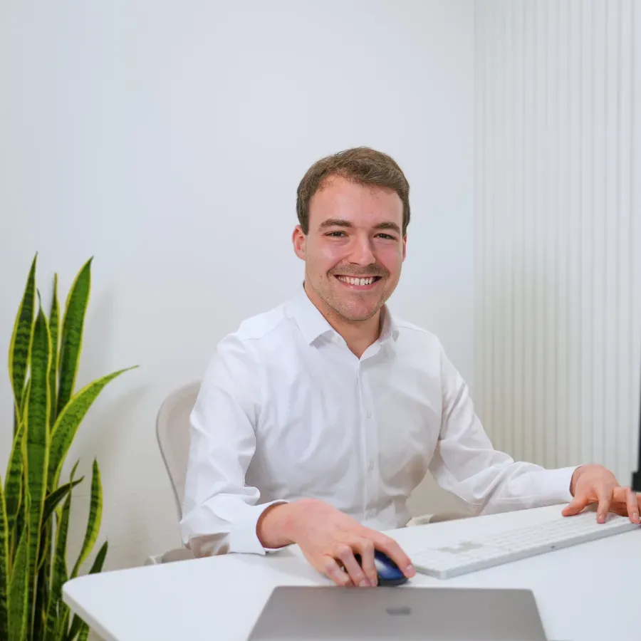 Man smiling at his desk while working on a computer in a bright, minimalist office.