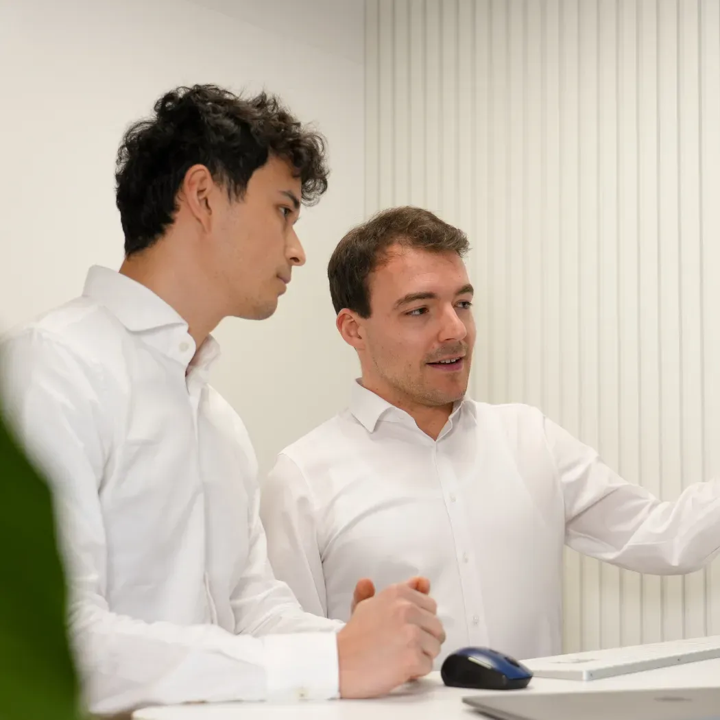 Zwei Kollegen stehen nebeneinander und besprechen Informationen, die auf einem Computerbildschirm angezeigt werden.