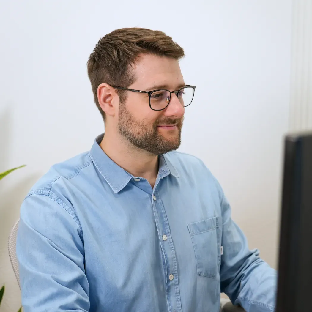 Mann in einem hellblauen Hemd, der in einer hellen, minimalistischen Büroumgebung am Computer arbeitet.