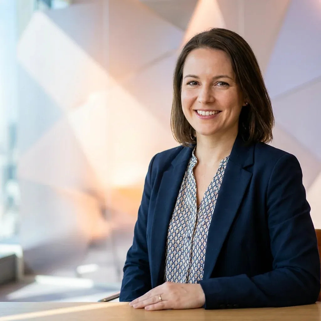 Smiling businesswoman in a blue blazer sitting at a desk in a modern office.