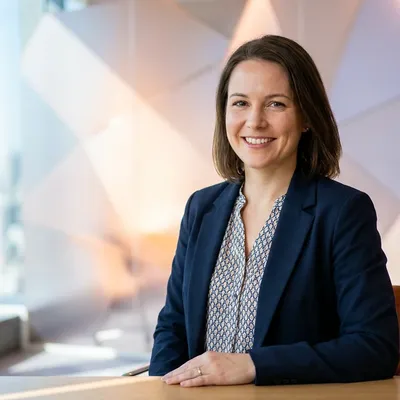 Smiling businesswoman in a blue blazer sitting at a desk in a modern office.