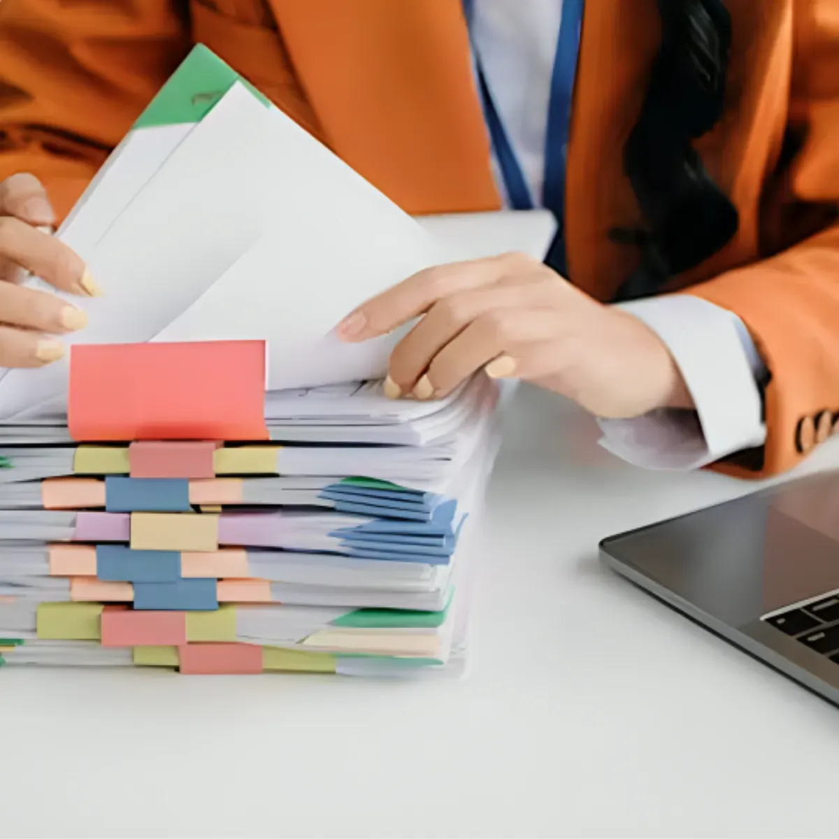 Person organizing a large stack of marked documents beside a laptop
