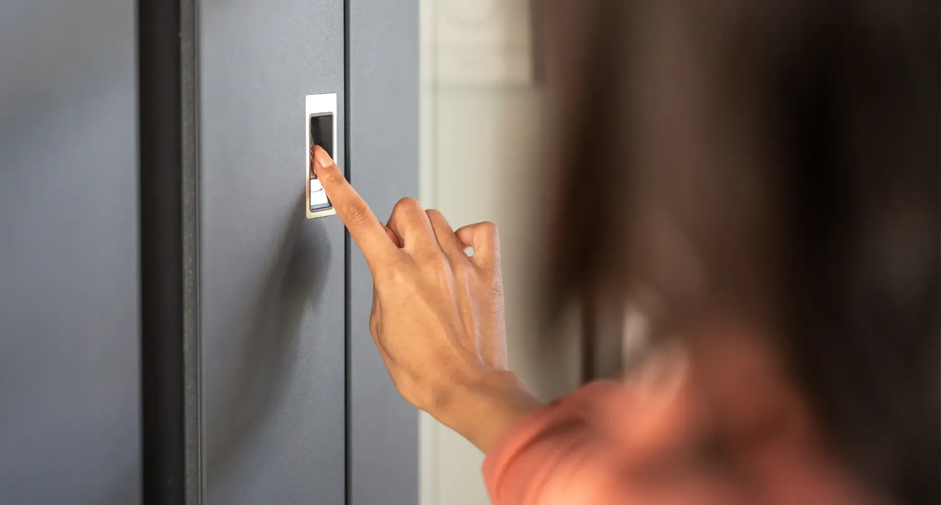 Person legt den Finger auf einen Fingerabdrucksensor zur Zugangskontrolle an einer Tür.