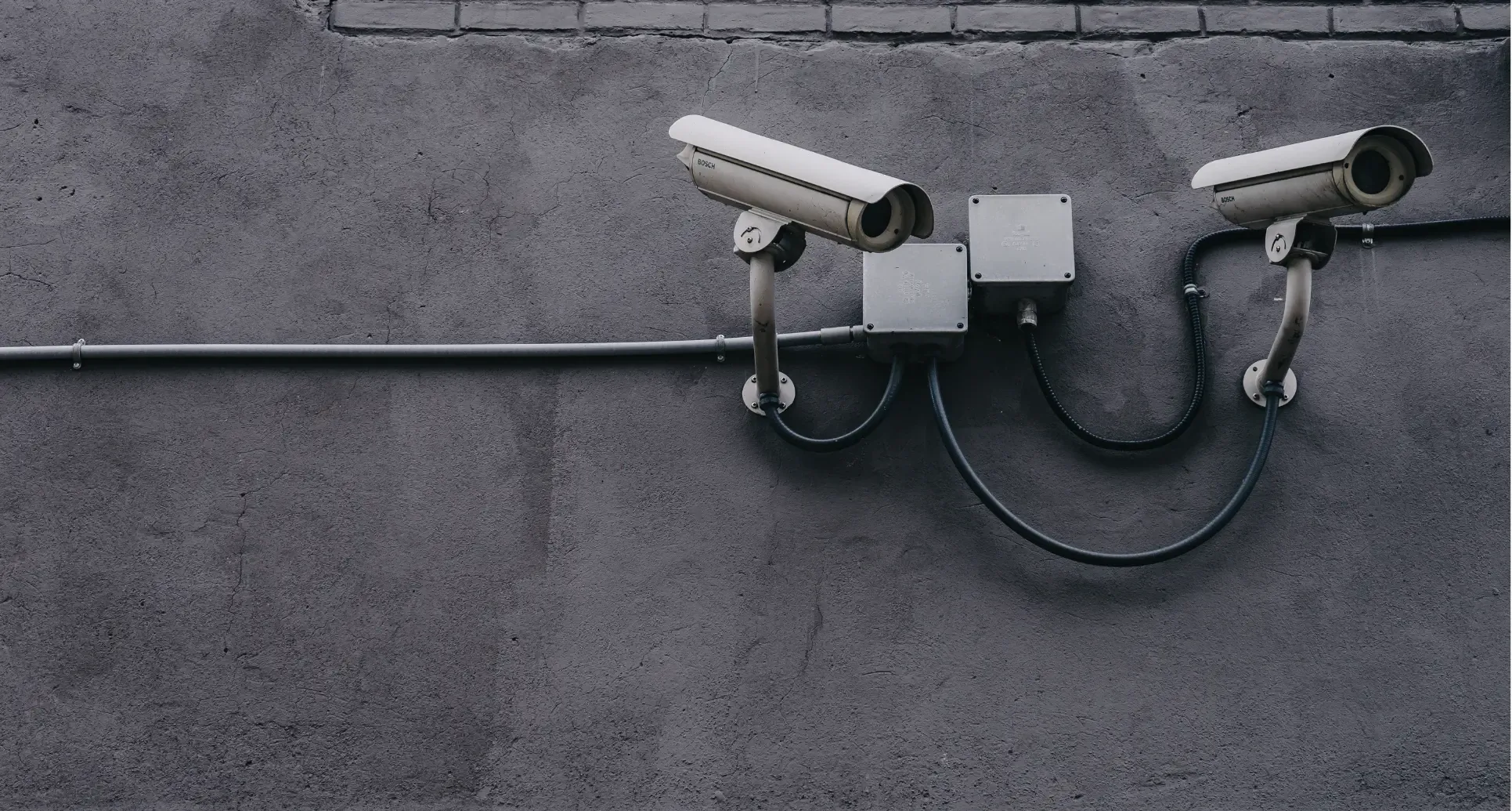 Two white security cameras mounted on a dark grey concrete wall.