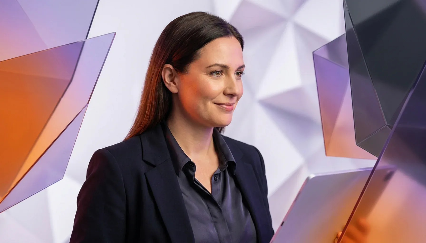 Smiling businesswoman holding a tablet against a modern, abstract geometric background.