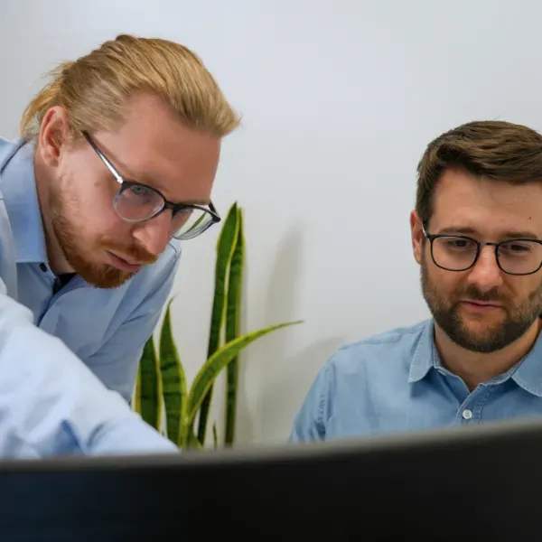 Zwei Männer in einem Büro, die sich auf einen Computerbildschirm konzentrieren, während sie etwas besprechen.