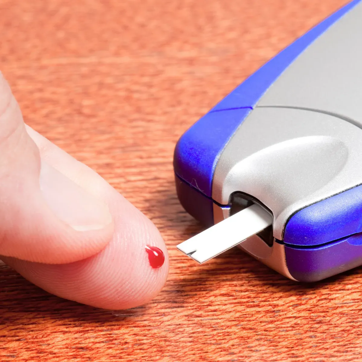 Finger mit Blutstropfen vor einem Blutzuckermessgerät