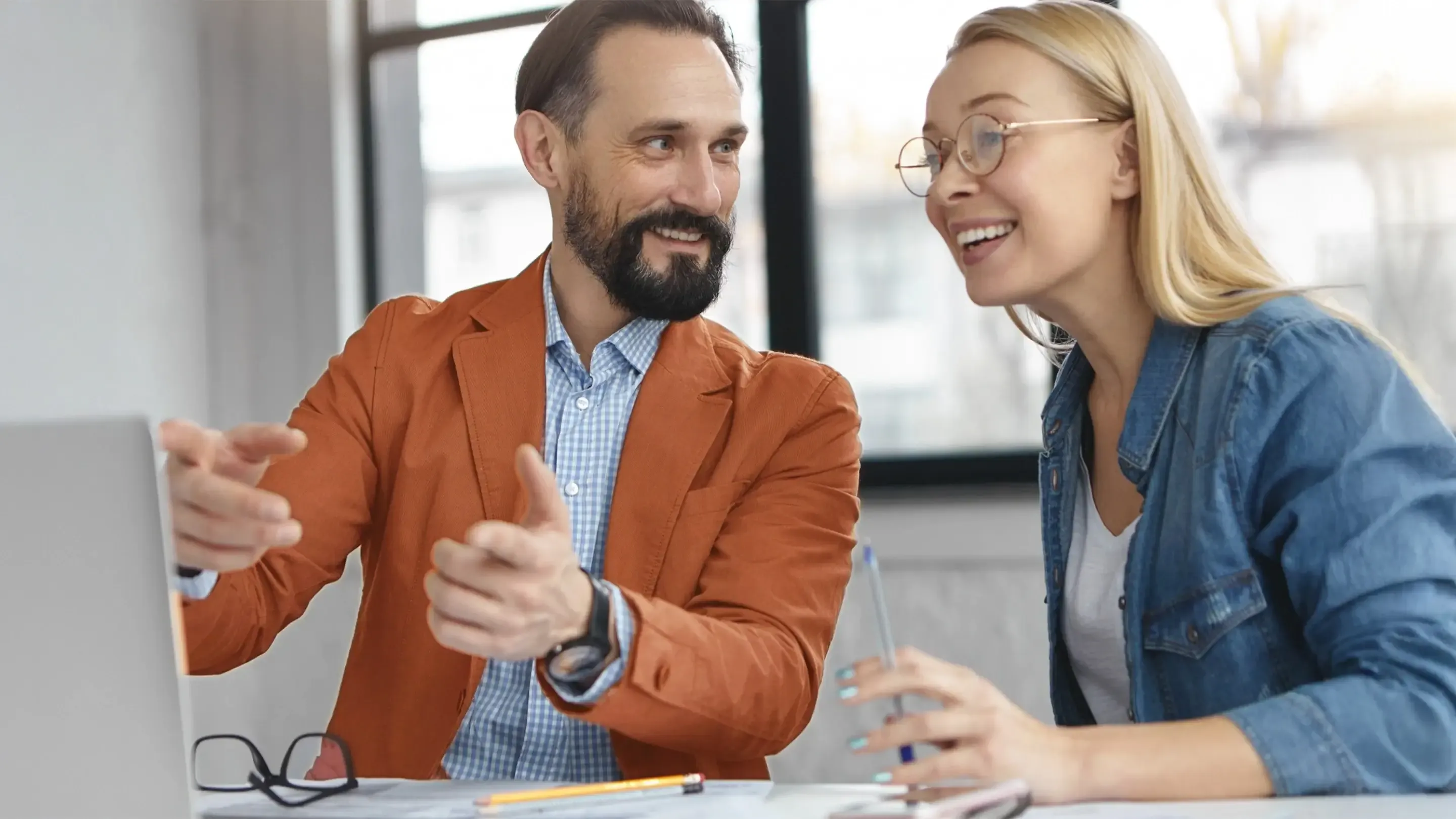 Ein Mann und eine Frau lächeln bei der Zusammenarbeit am Laptop.