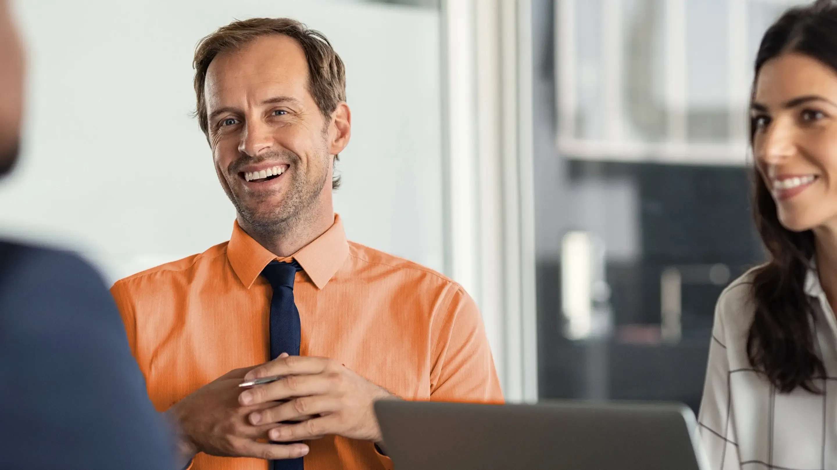 A smiling man in an orange shirt during a business meeting.