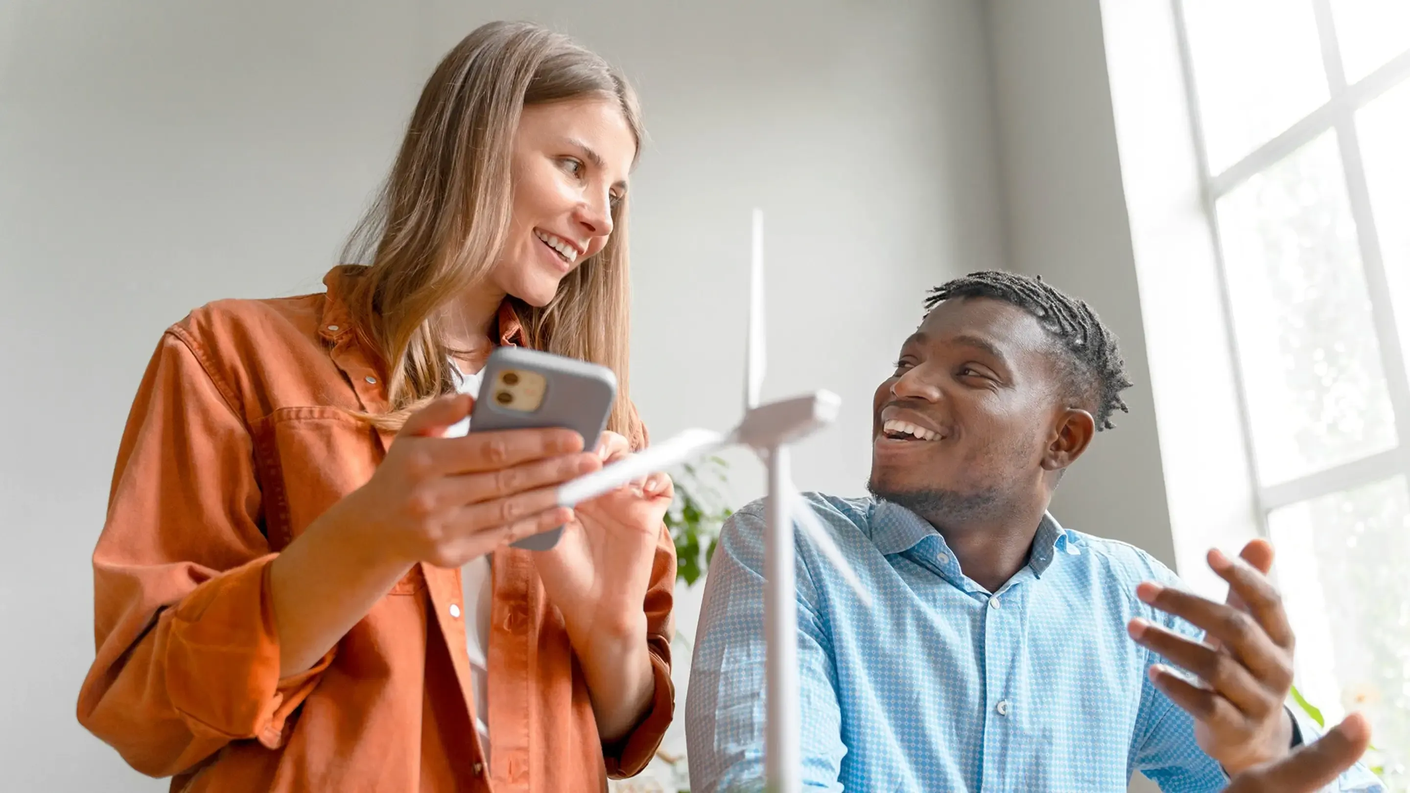 A man and woman smile, discussing a model wind turbine.