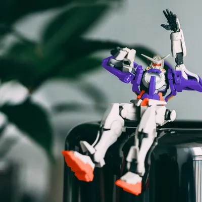 Small colorful robot figure sits on a black object and playfully raises its arms