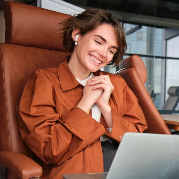 Lächelnde Person mit Kopfhörern führt einen Videoanruf am Laptop.